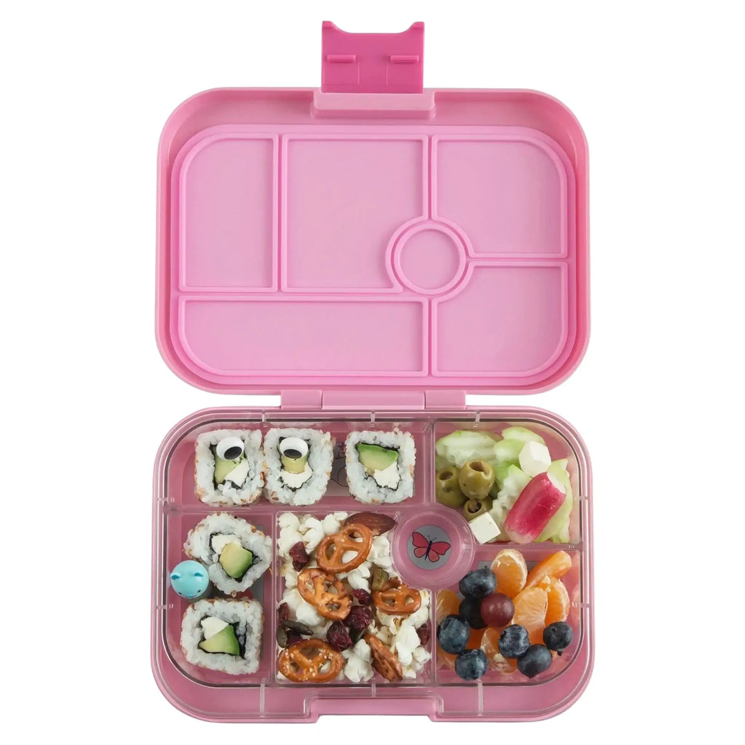 Roze bento lunchbox voor kinderen, gevuld met sushi, groenten, fruit en pretzels.