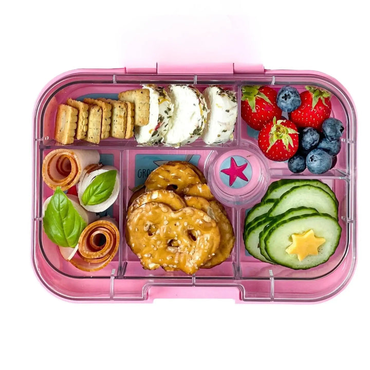 Lunchtrommel met crackers, geitenkaasrolletjes, aardbeien, blauwe bessen, pretzels, komkommer en hamrolletjes.