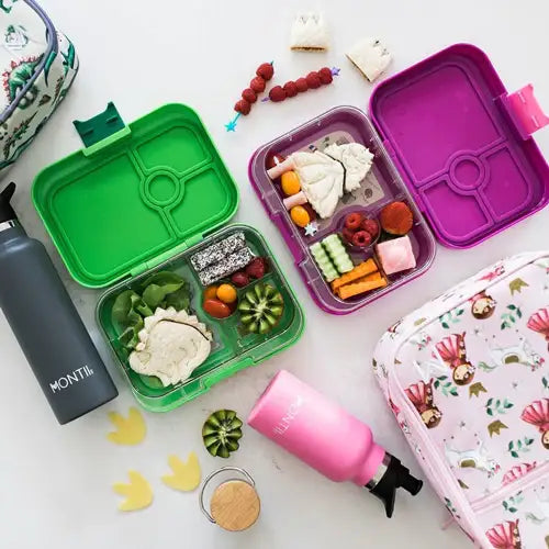 Kleurrijke lunchboxen met gezonde kinderhapjes, waterfles en broodtrommel op tafel