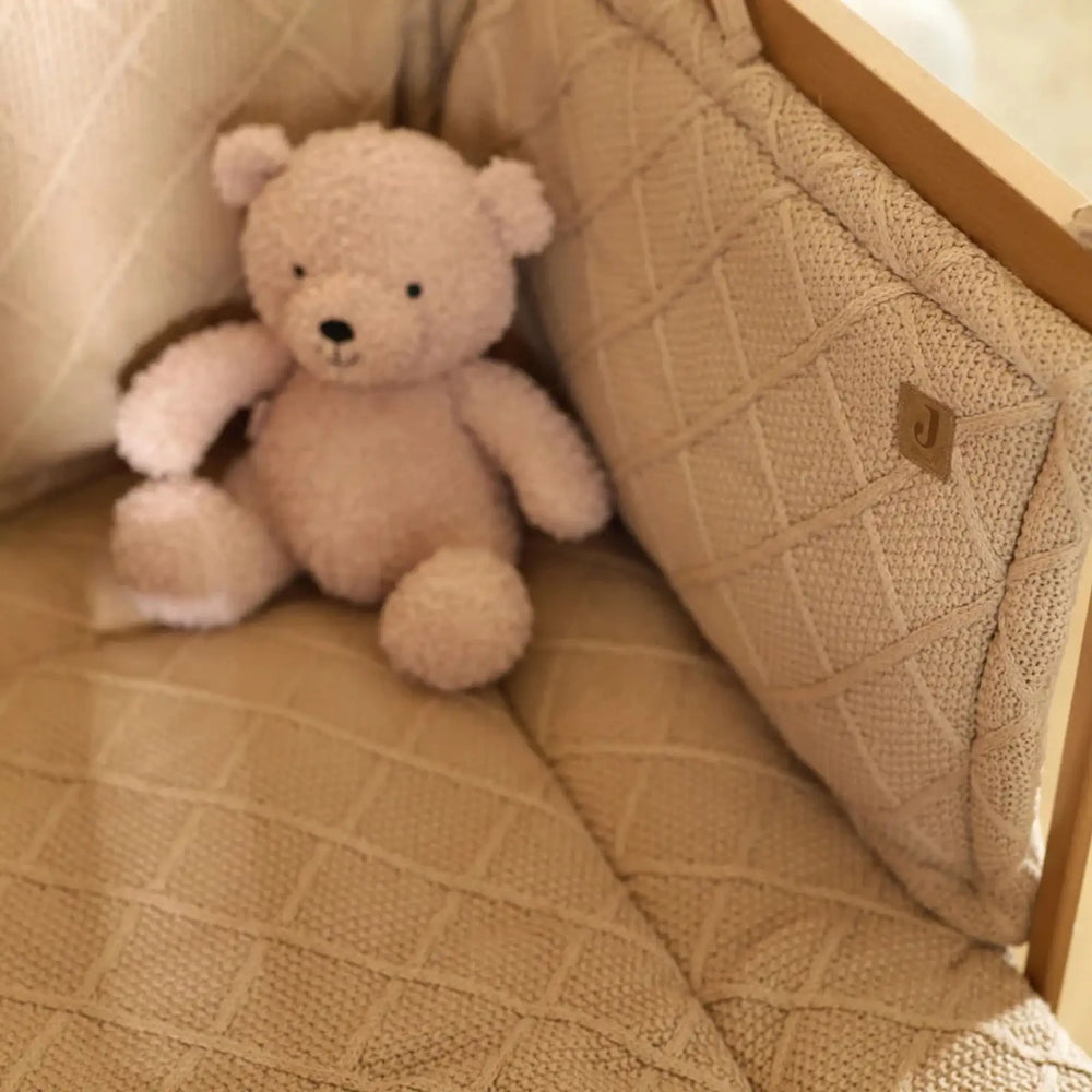 Zacht beige teddybeer knuffel op gebreide kinderstoel met ruitpatroon, babykamer decoratie